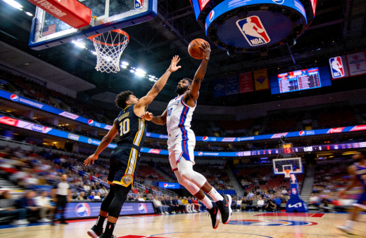 NBA篮球比赛现场，球员在三分线外起跳投篮，防守球员伸手干扰